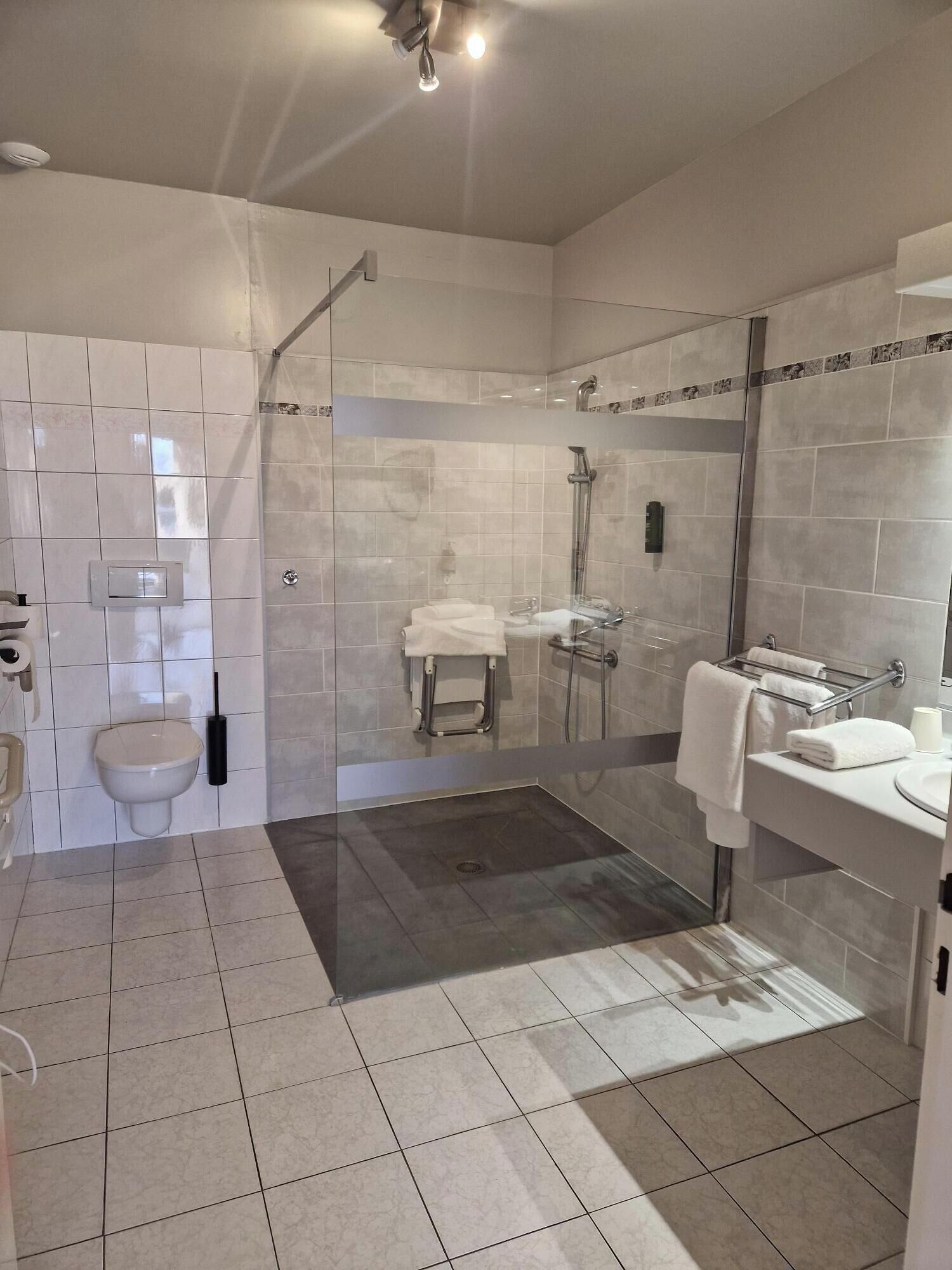 Un baño moderno con ducha de vidrio, inodoro y lavamanos con toallero.