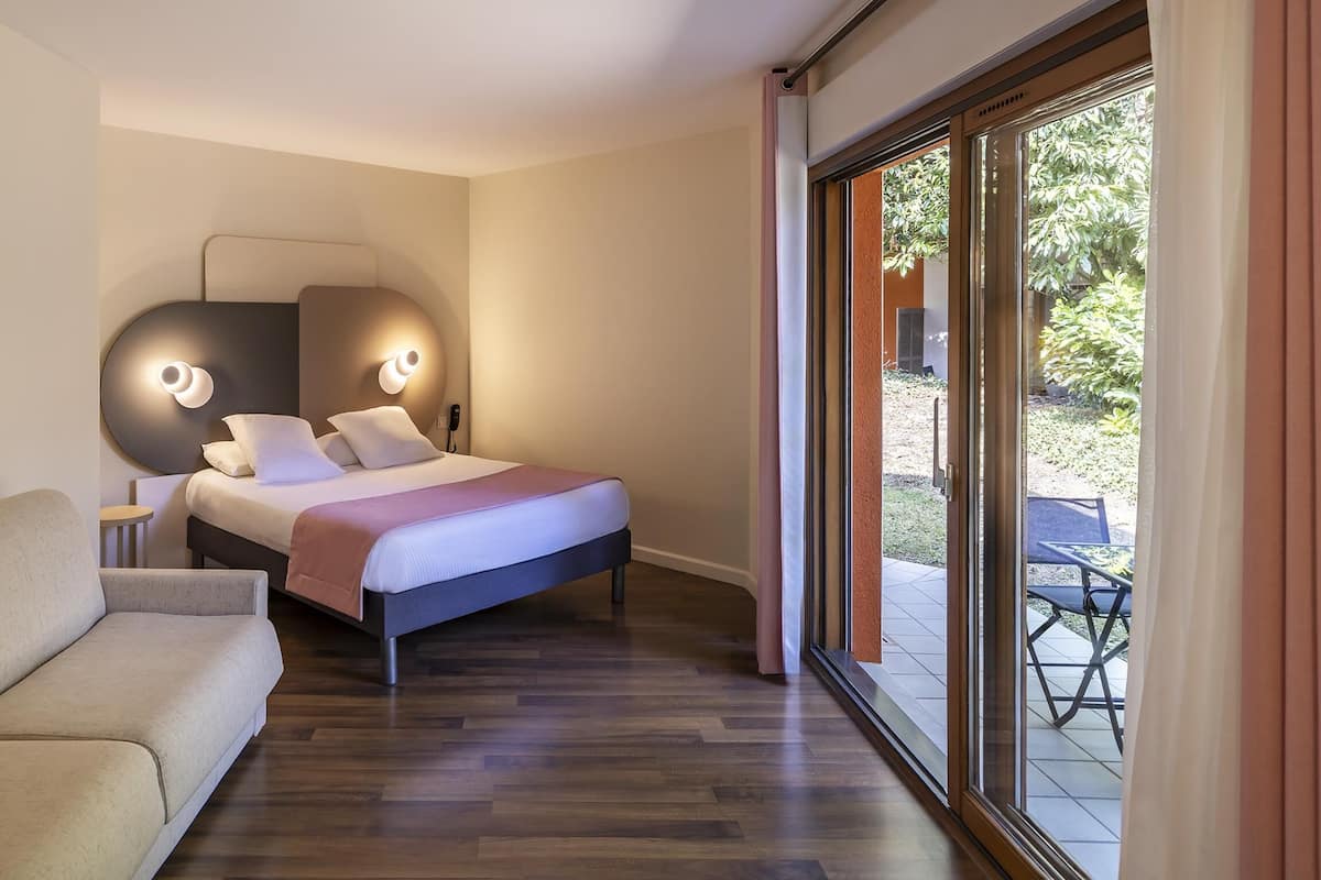 A modern bedroom with a bed, a sofa, and a large window with a view of the outdoors.
