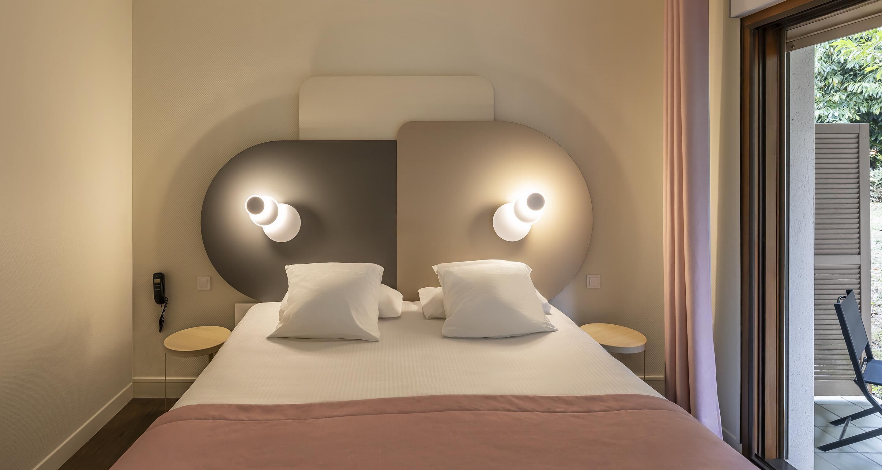 A modern bedroom with a large bed, bedside tables, and a phone on the wall.