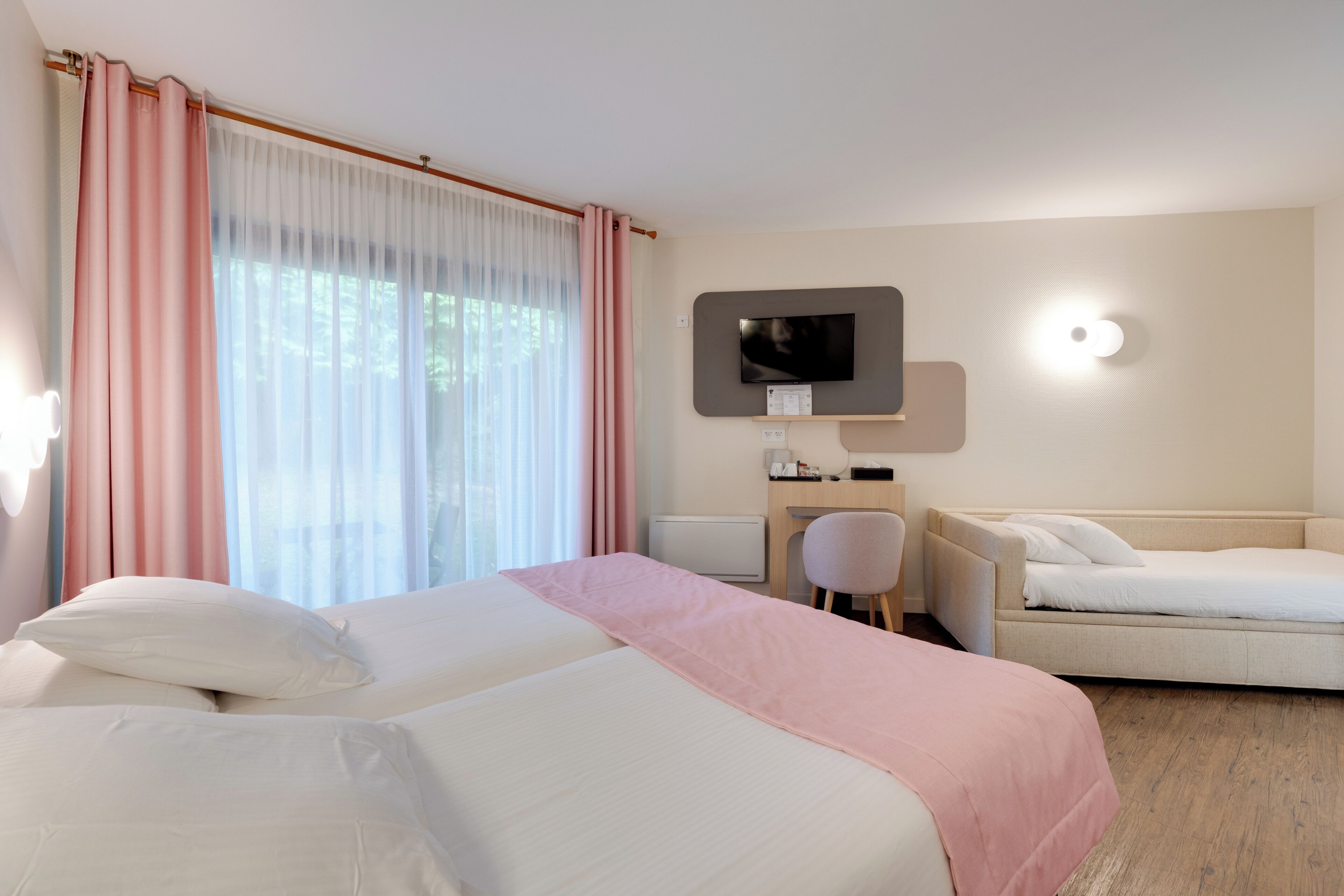 Habitación de hotel con cama, escritorio, silla, televisor y ventana con cortinas.