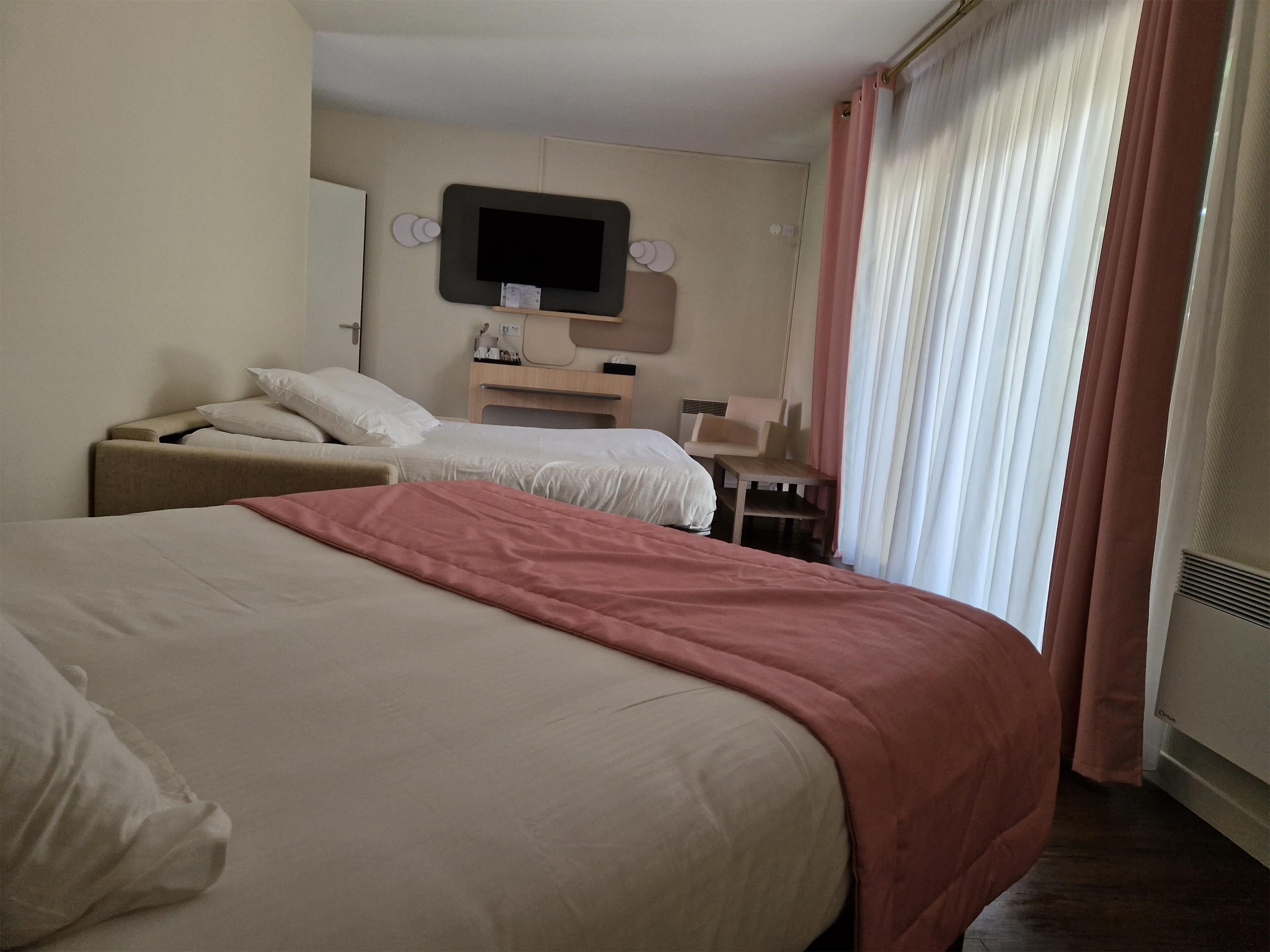 Habitación de hotel con dos camas, un televisor montado en la pared, una mesita y una silla.