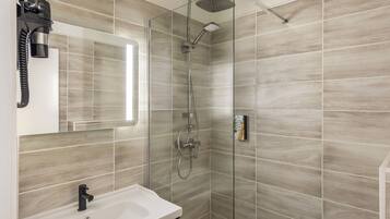 A modern bathroom with a glass shower enclosure, a white sink, and a handheld showerhead.