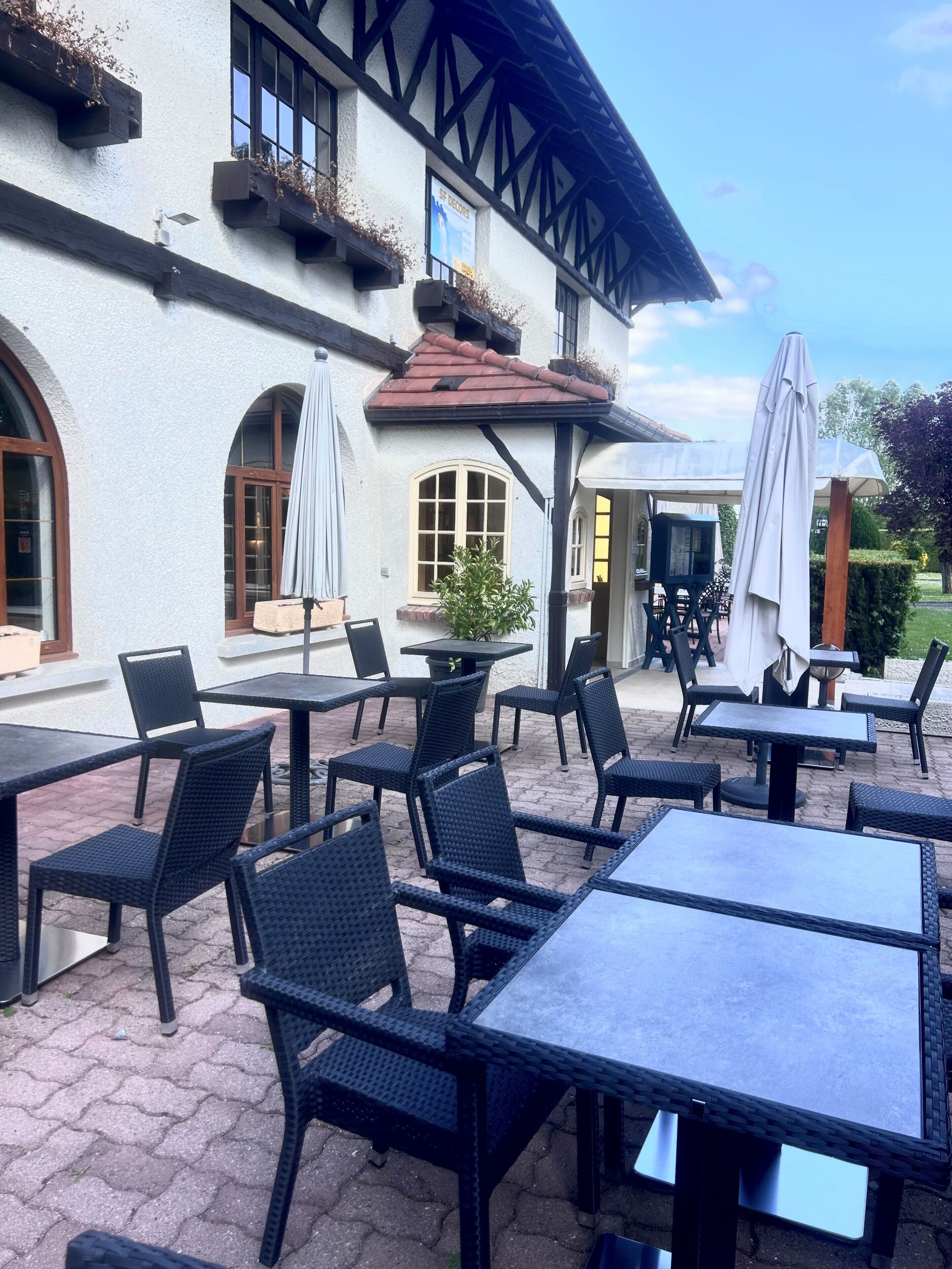 An outdoor patio with tables and chairs, a building with a white facade and dark wooden beams, and a covered area with umbrellas.