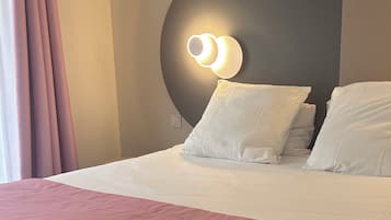 A neatly made bed with white and pink bedding, a round wall-mounted light fixture, and a window with curtains.