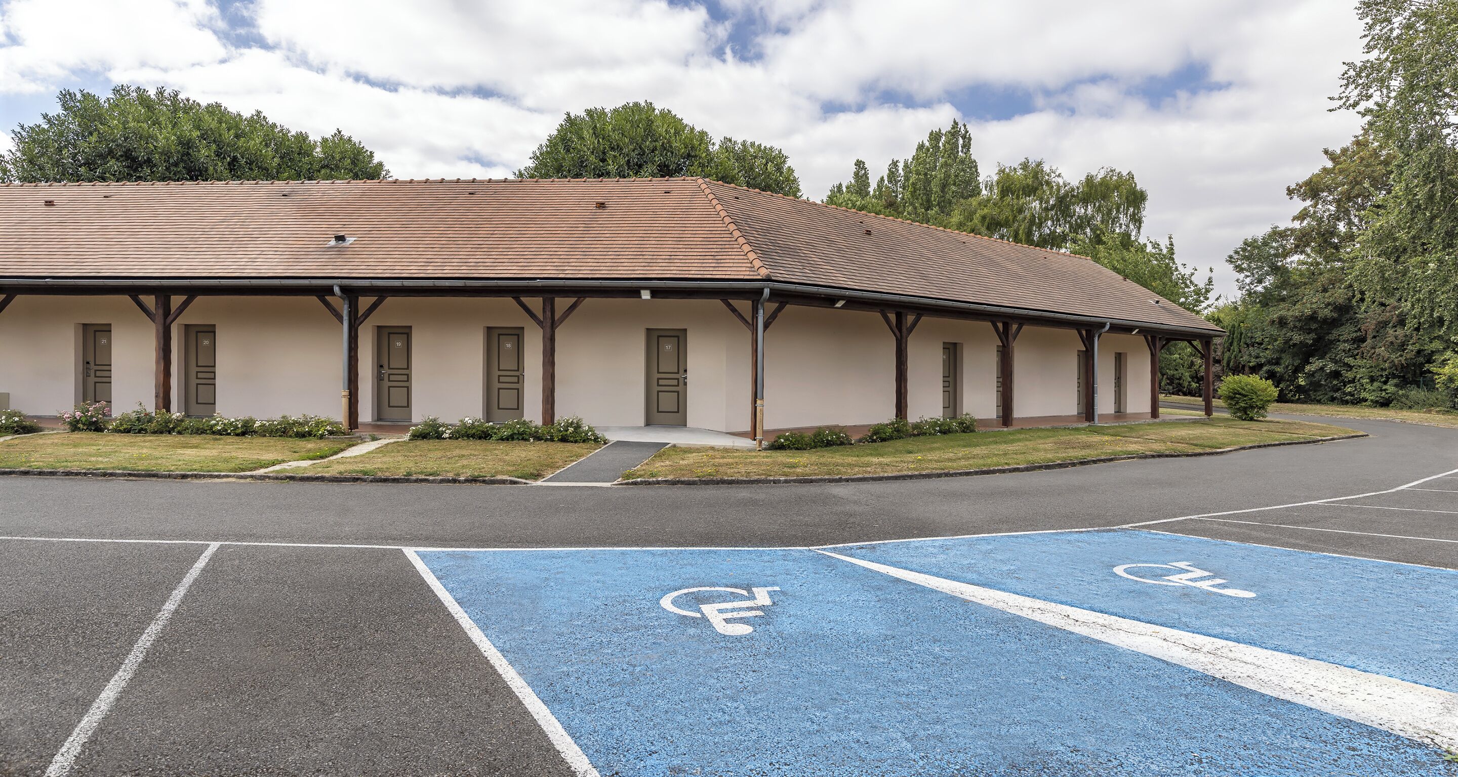Un edificio con techo plano, varias puertas y un estacionamiento con espacios reservados para personas con discapacidad, señalizados en azul.