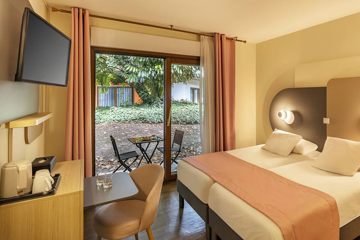 A hotel room with a bed, bedside table, chair, and a TV mounted on the wall.