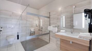 A modern bathroom with a glass-enclosed shower, a toilet, a sink with a mirror, and a hairdryer on the counter.