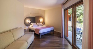 A modern bedroom with a bed, a sofa, a wall-mounted light fixture, and a sliding glass door leading to an outdoor area. - Sure Hotel by Best Western Saint-Quentin Ouest Le pot d'étain (Holnon)