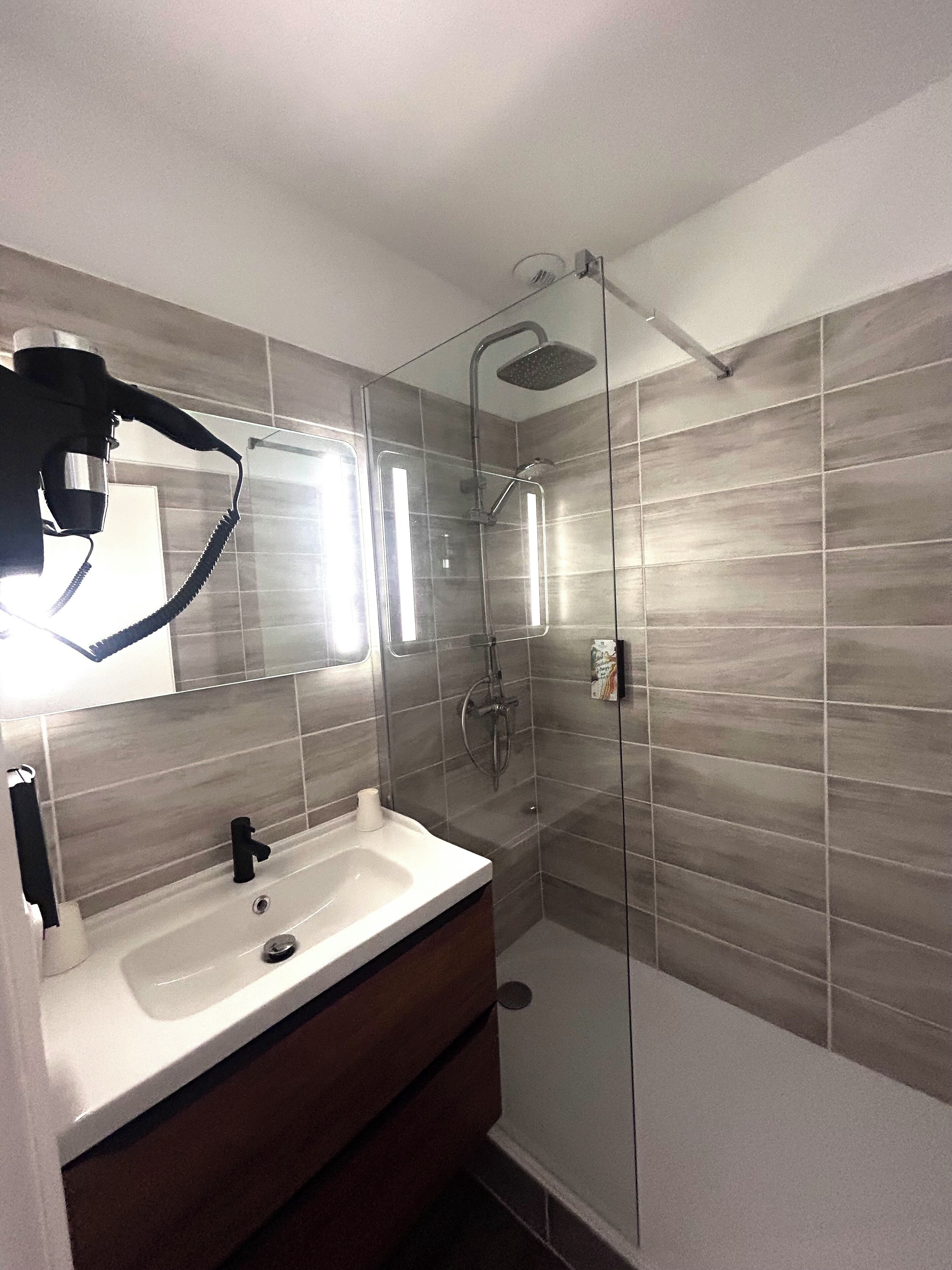 Un baño moderno con ducha acristalada, un lavabo blanco y un espejo.