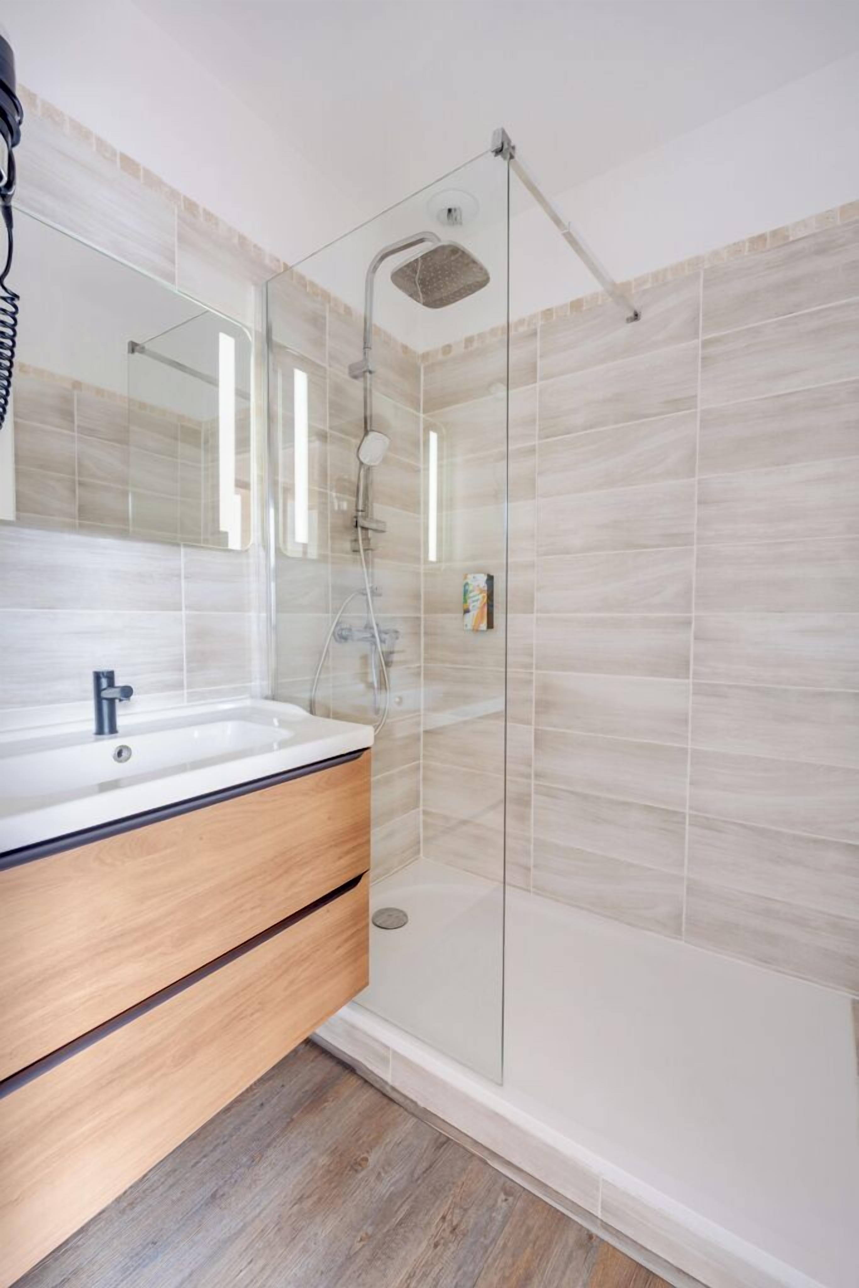 A modern bathroom with a glass shower enclosure, a wooden vanity, and a large mirror.