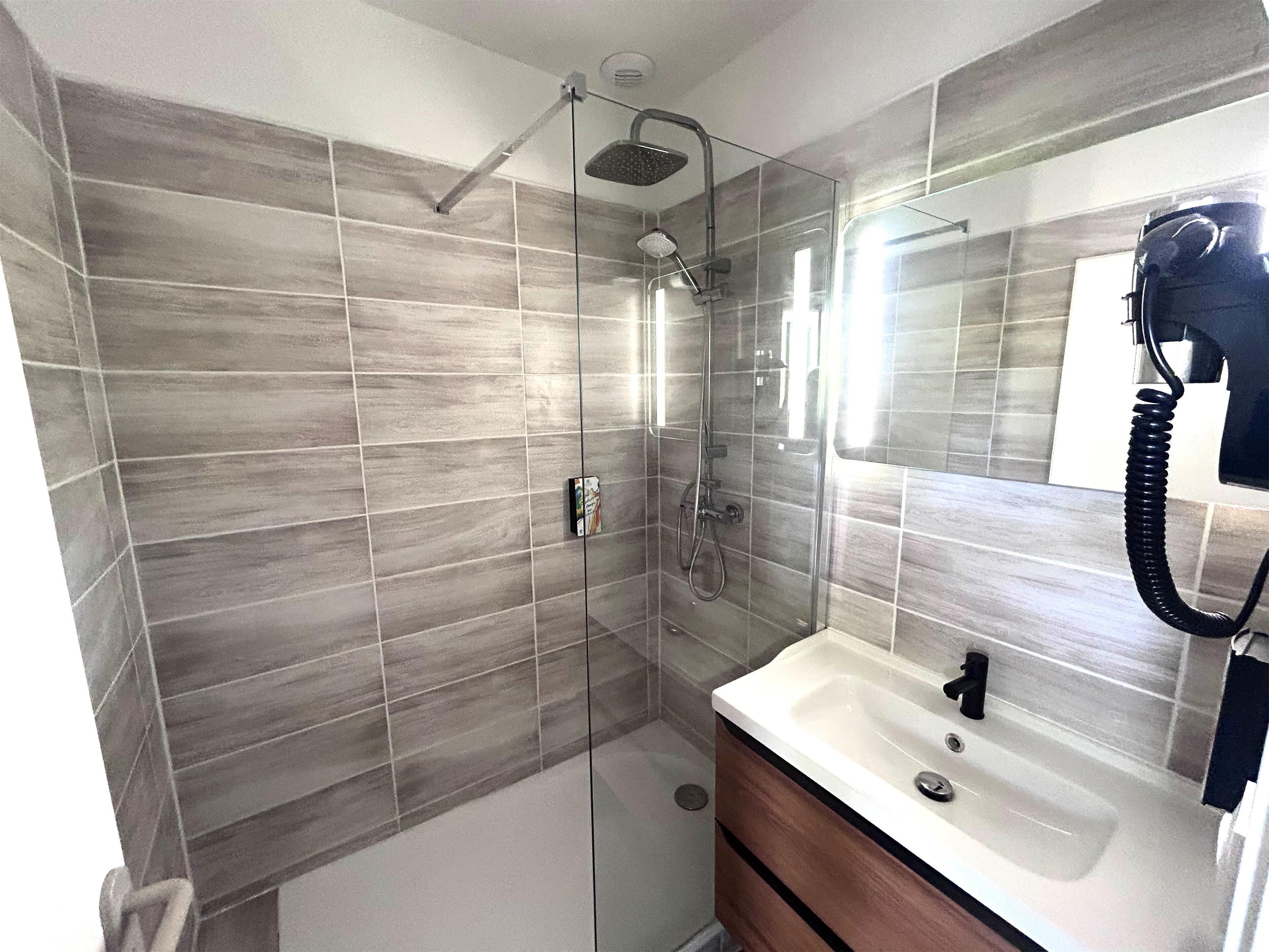 A modern bathroom with a glass shower enclosure, a white sink with a black faucet, and a large mirror.