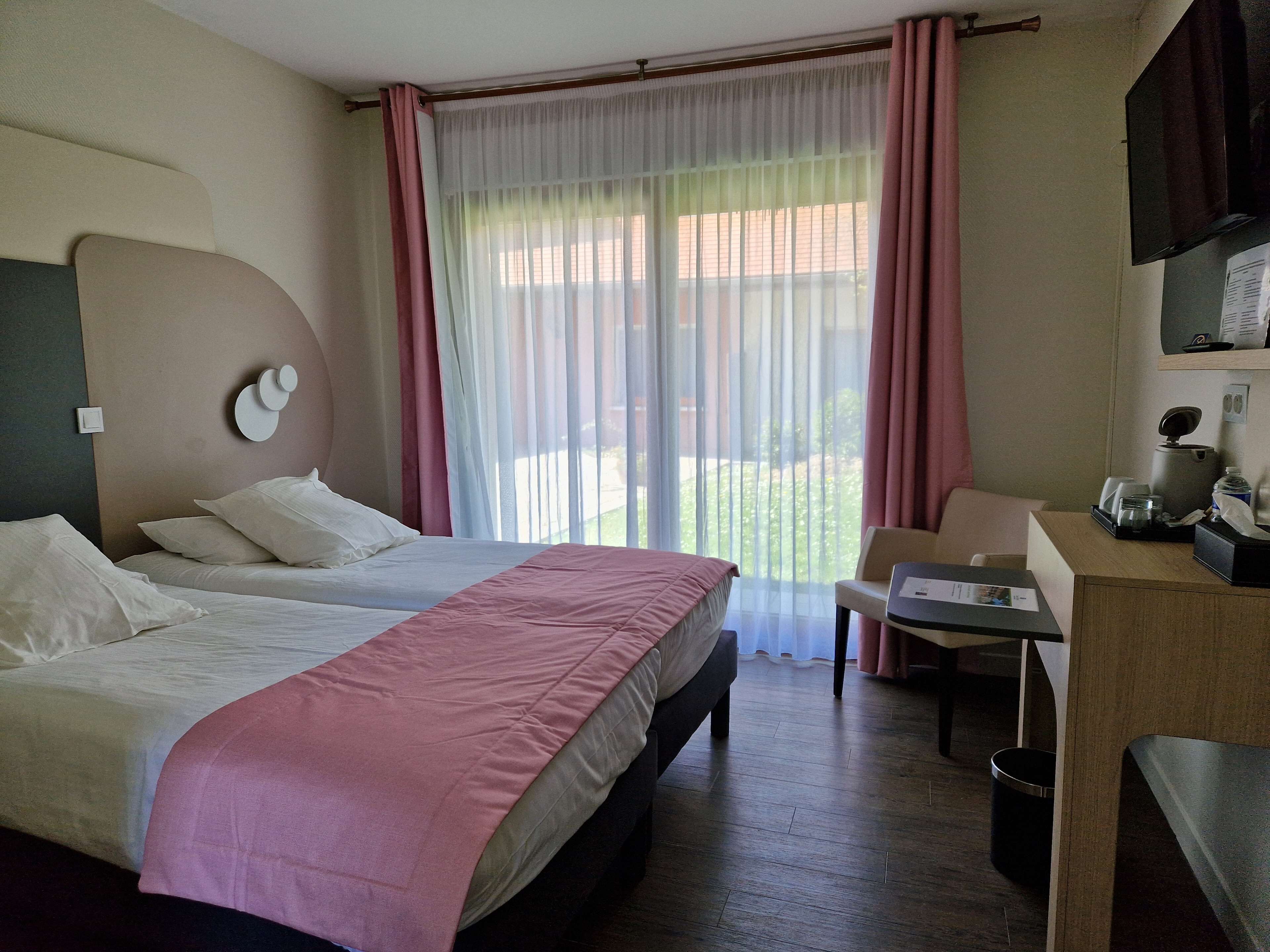 Een hotelkamer met een bed, een bureau, een stoel, een televisie en een raam met gordijnen.