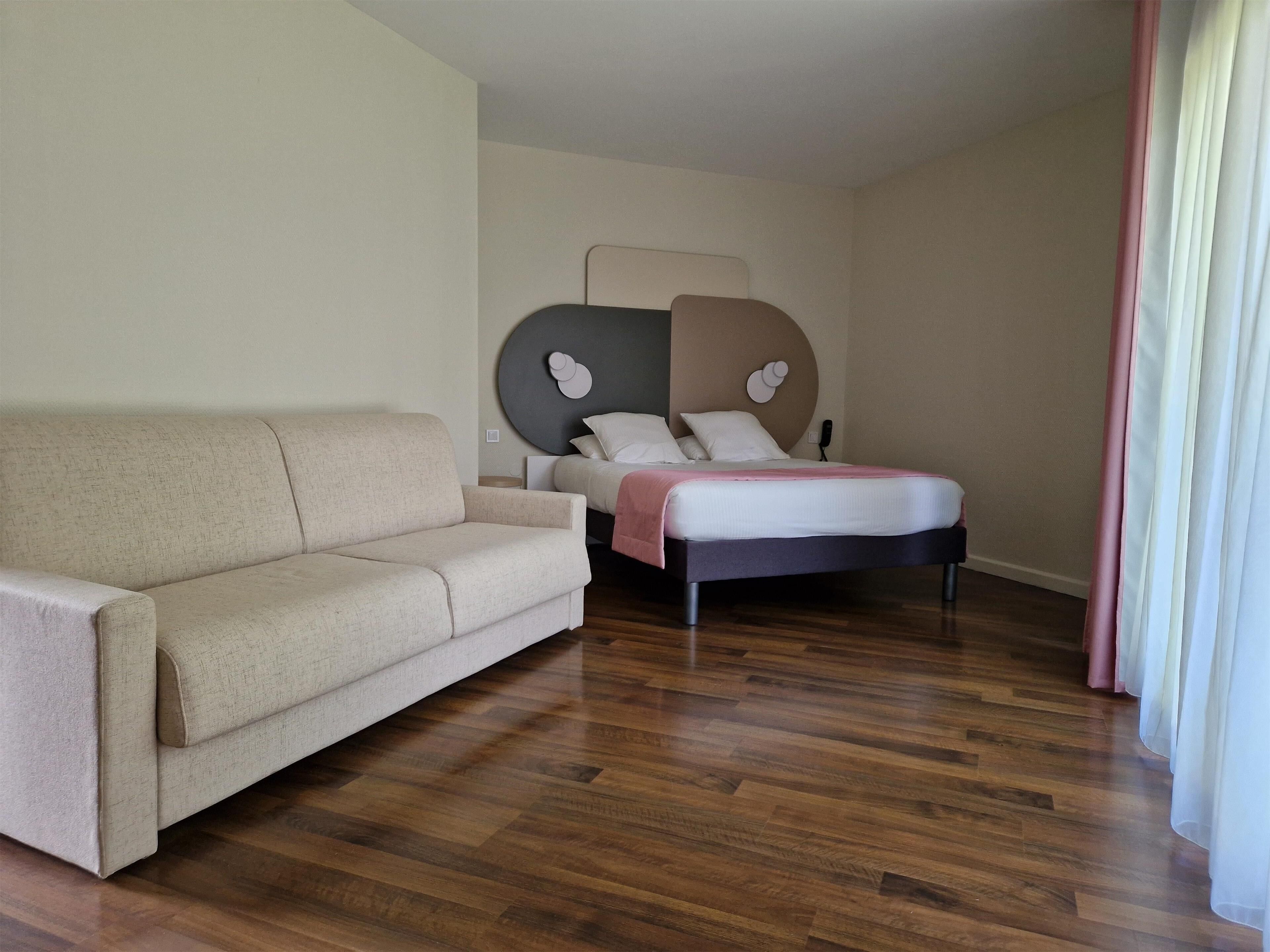 A hotel room with a bed, a sofa, and a wooden floor.