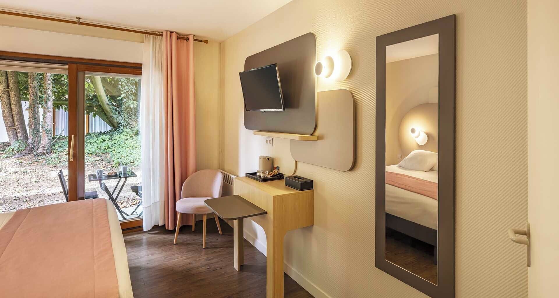 Une chambre d’hôtel équipée d’un lit, d’un bureau, d’une chaise, d’une télévision et d’un grand miroir.