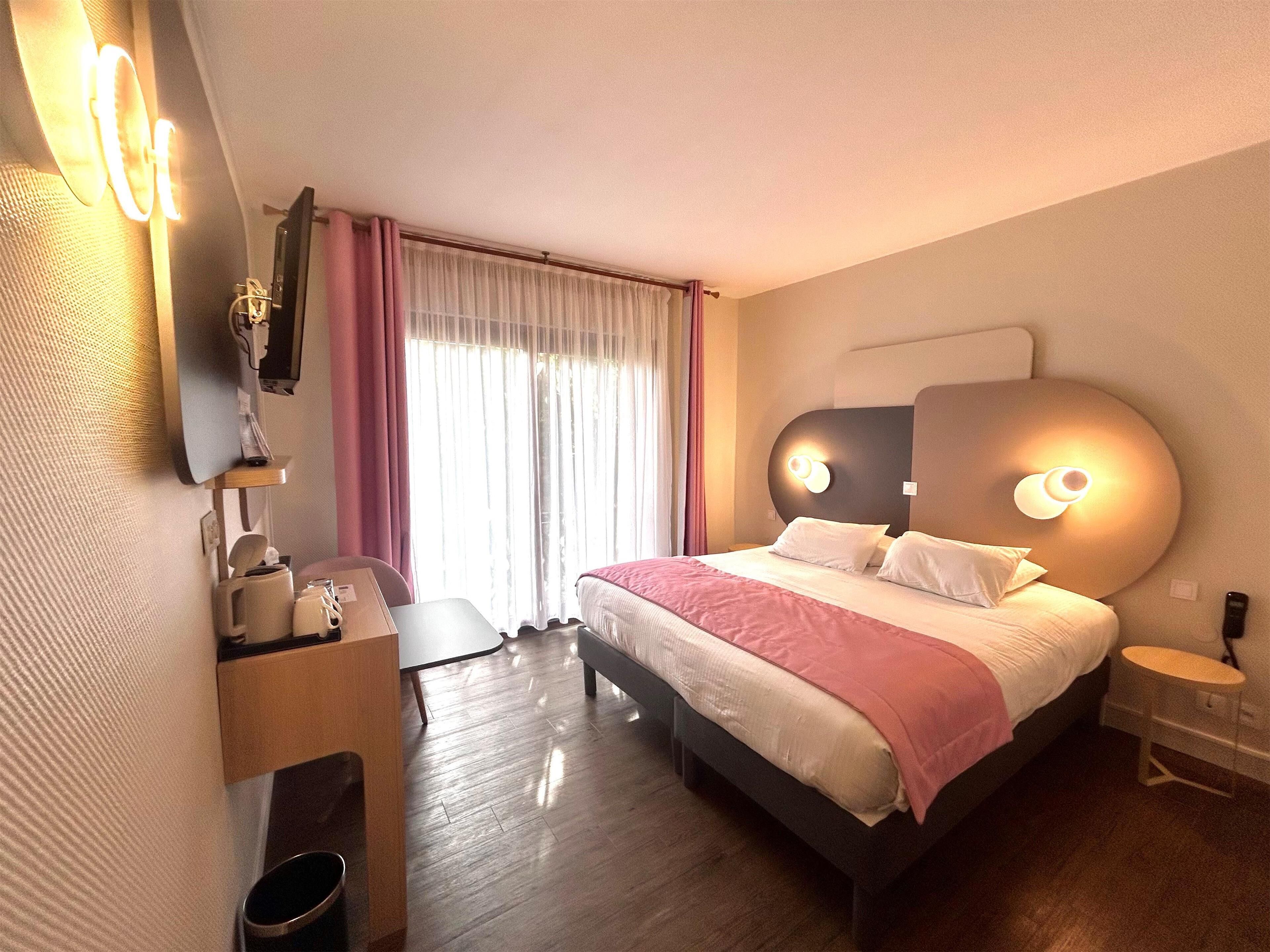 A modern hotel room with a large bed, bedside tables, a desk, and a mirror.