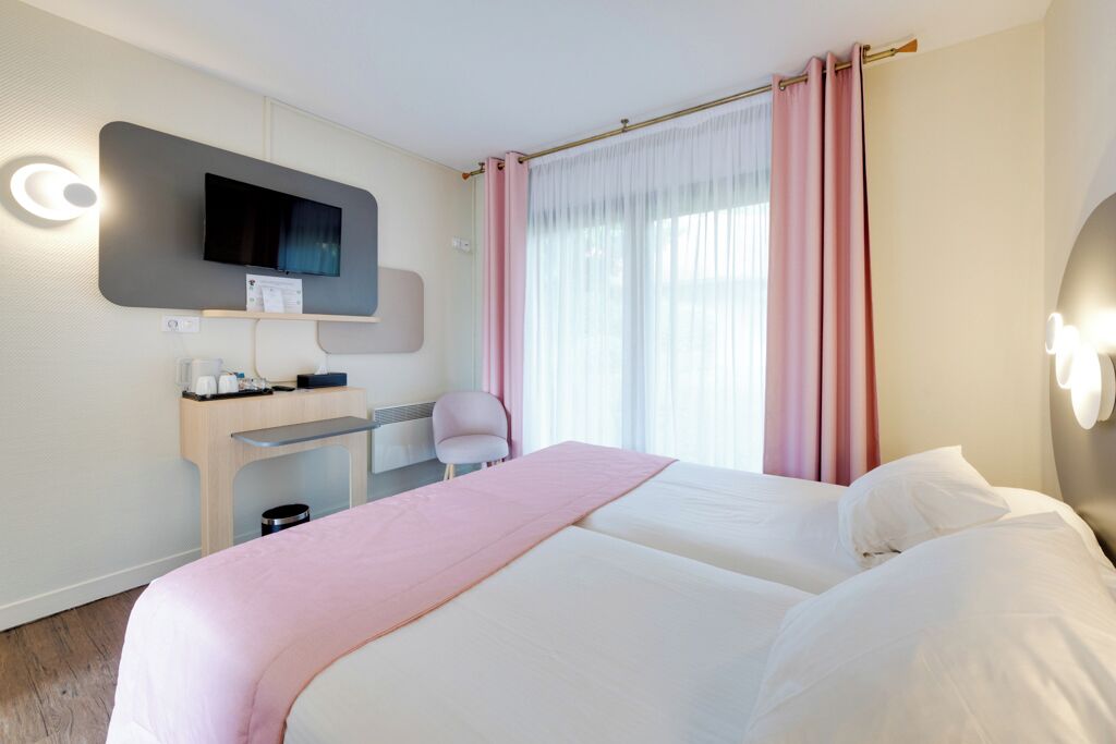 Habitación de hotel con dos camas, un escritorio, una silla, un televisor y una ventana con cortinas.