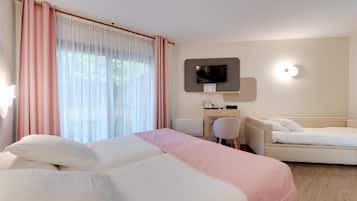 Habitación de hotel con dos camas, un escritorio, una silla, un televisor y un ventanal con cortinas.