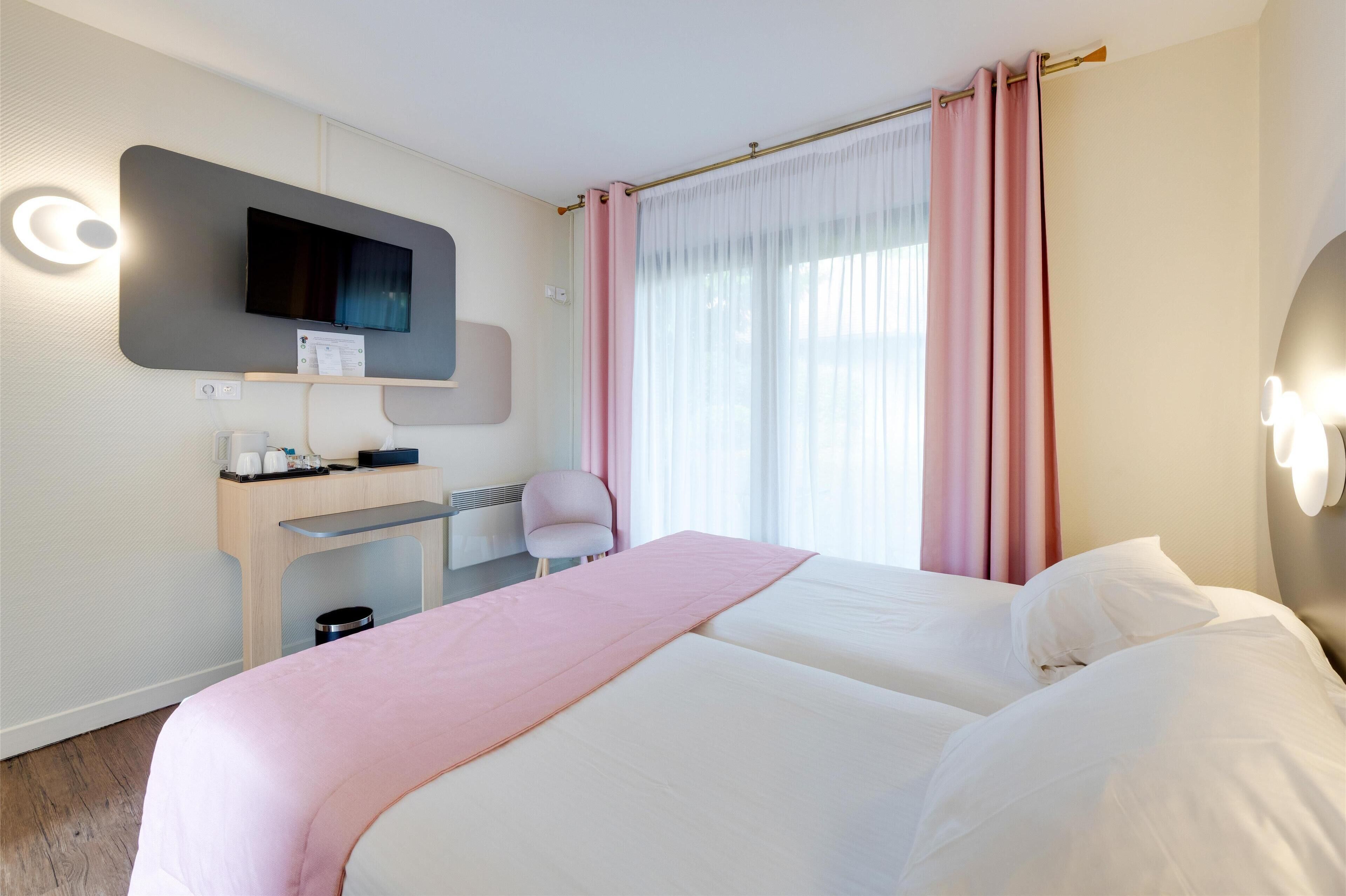 Habitación de hotel con dos camas, un escritorio, una silla, un televisor y una ventana con cortinas.