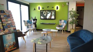 A modern lounge area with seating, a wall-mounted TV, and a plant.