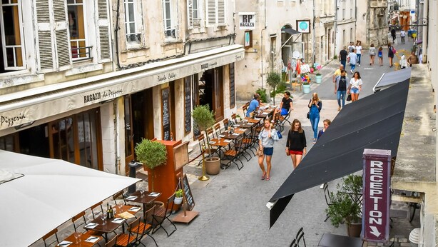 A street with outdoor seating, buildings with shutters, and a sign for a restaurant.