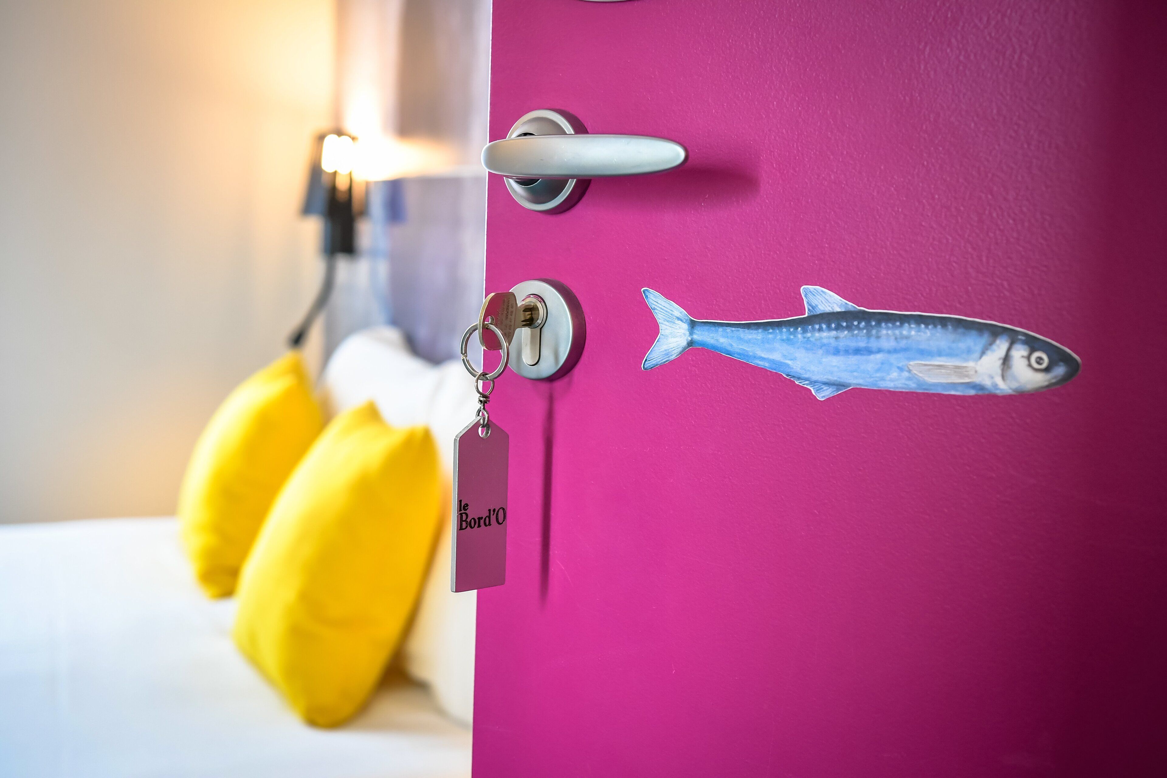 A pink door with a keyhole, a key, a keychain with a tag, and a fish decal.
