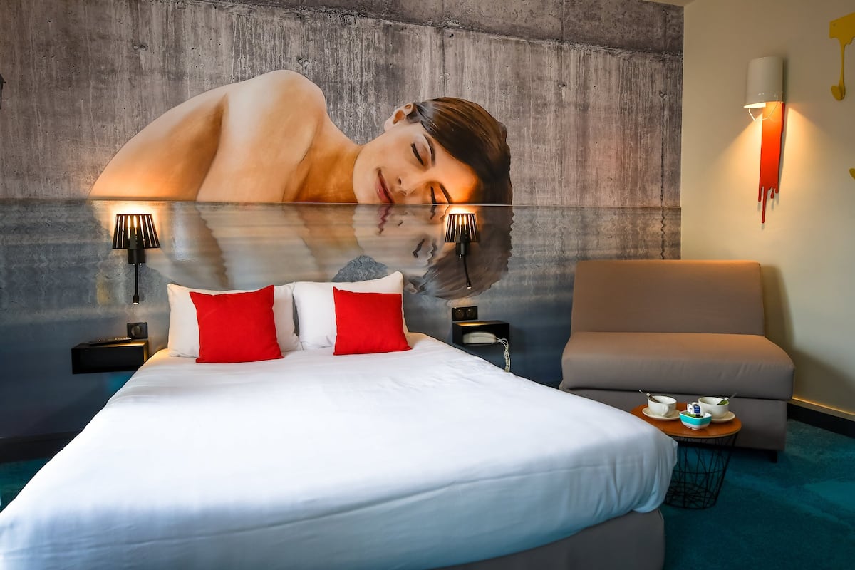 Une chambre d’hôtel moderne avec un grand lit, un canapé, une petite table avec un service à thé et un luminaire fixé au mur.