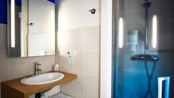 Un baño con un lavamanos blanco, un espejo y una cabina de ducha de cristal.