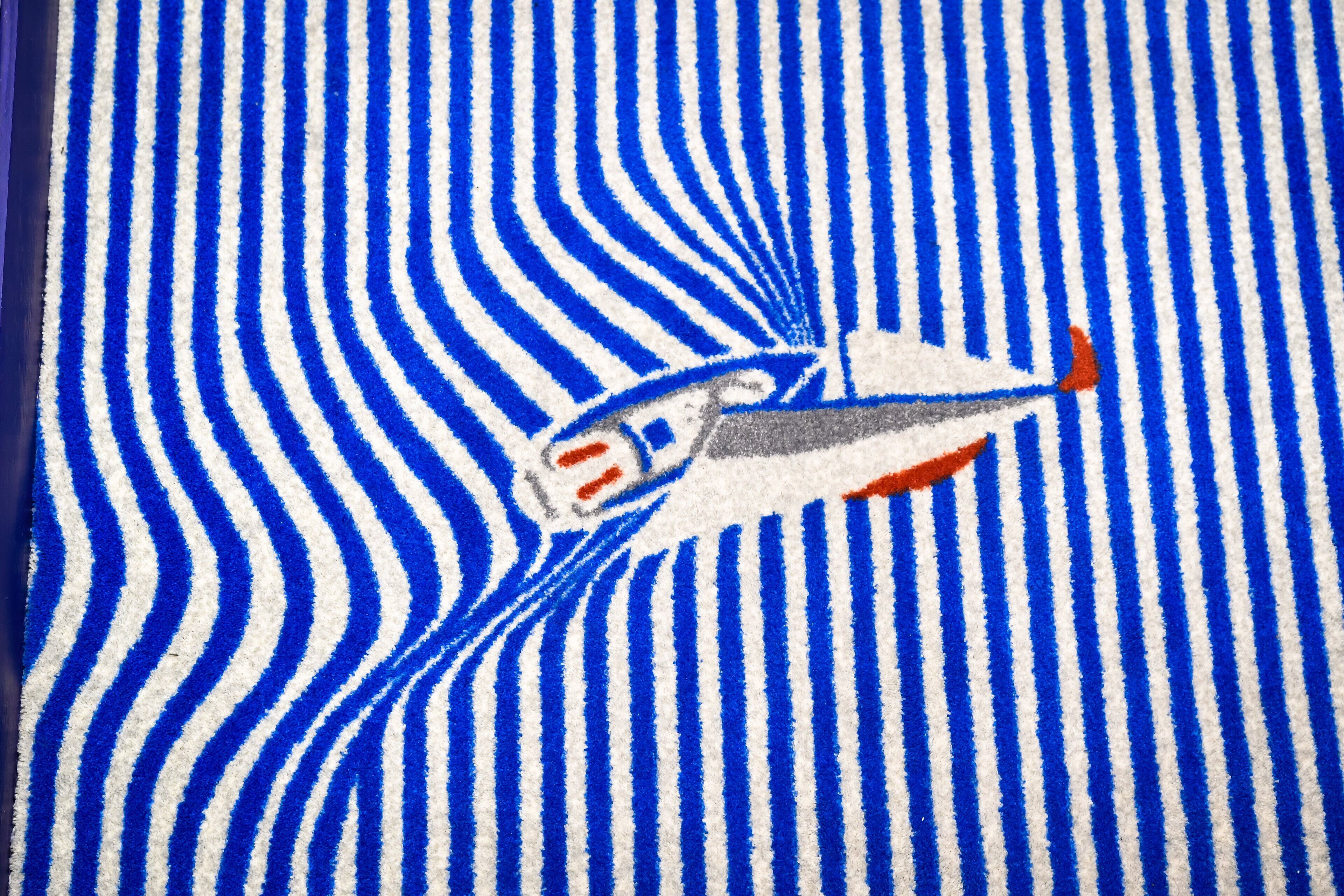 A striped carpet with a central design of a white and red airplane.