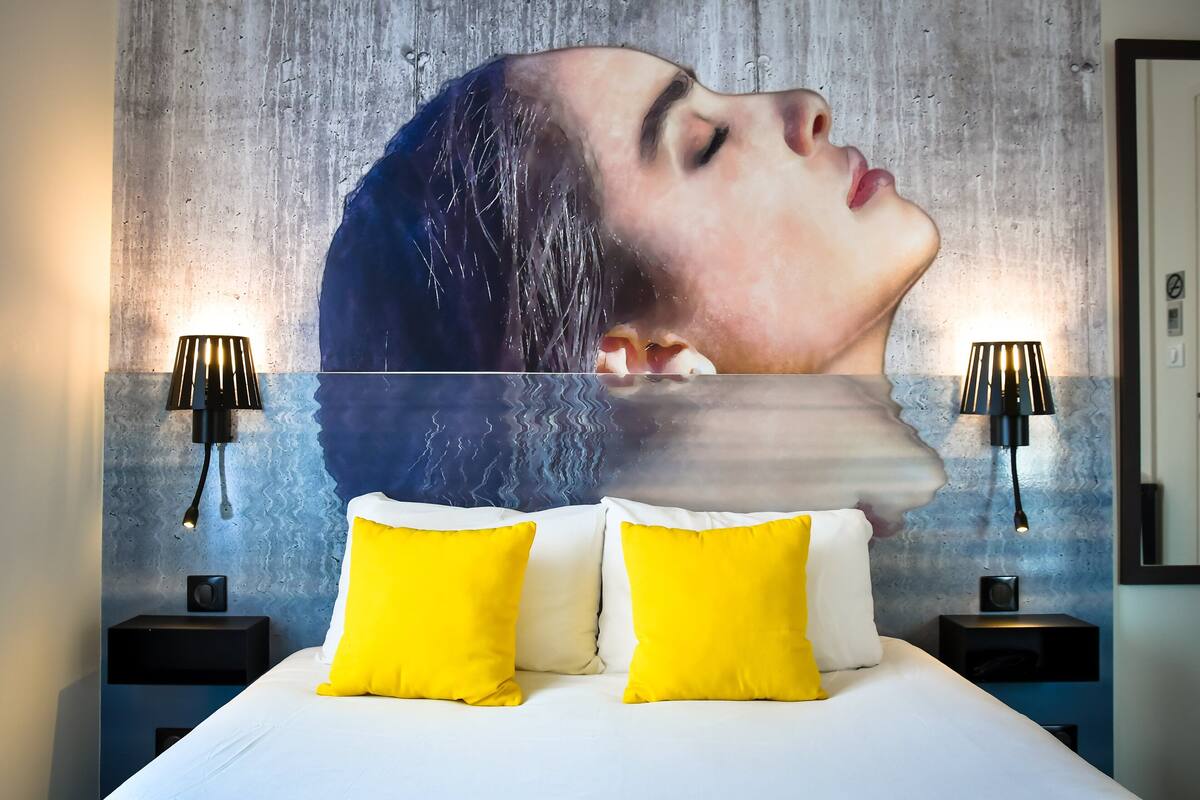 Une chambre à coucher avec un lit, deux oreillers jaunes, un oreiller blanc et un mur orné d’un motif texturé.
