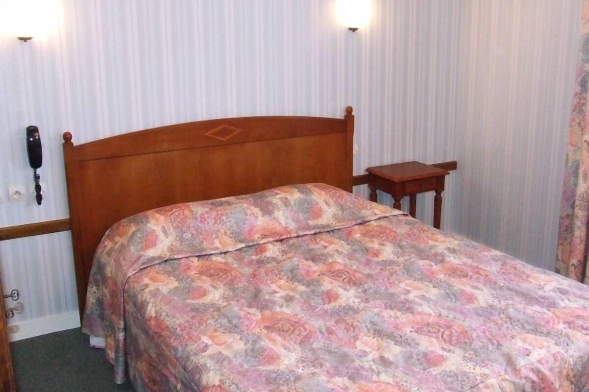 Une chambre à coucher avec un lit en bois, une table de chevet et deux lampes fixées au mur.