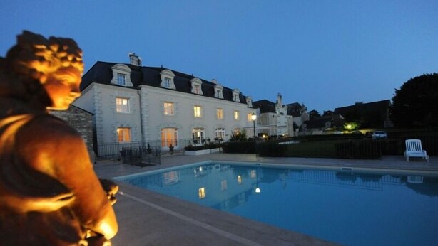 A large building with a swimming pool, a statue, and a well-lit entrance.