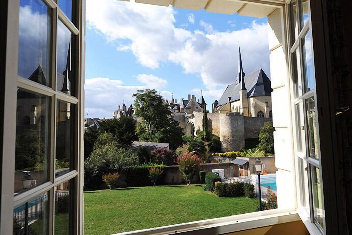 Une vue depuis une fenêtre donnant sur un château, avec une pelouse bien entretenue et une piscine.