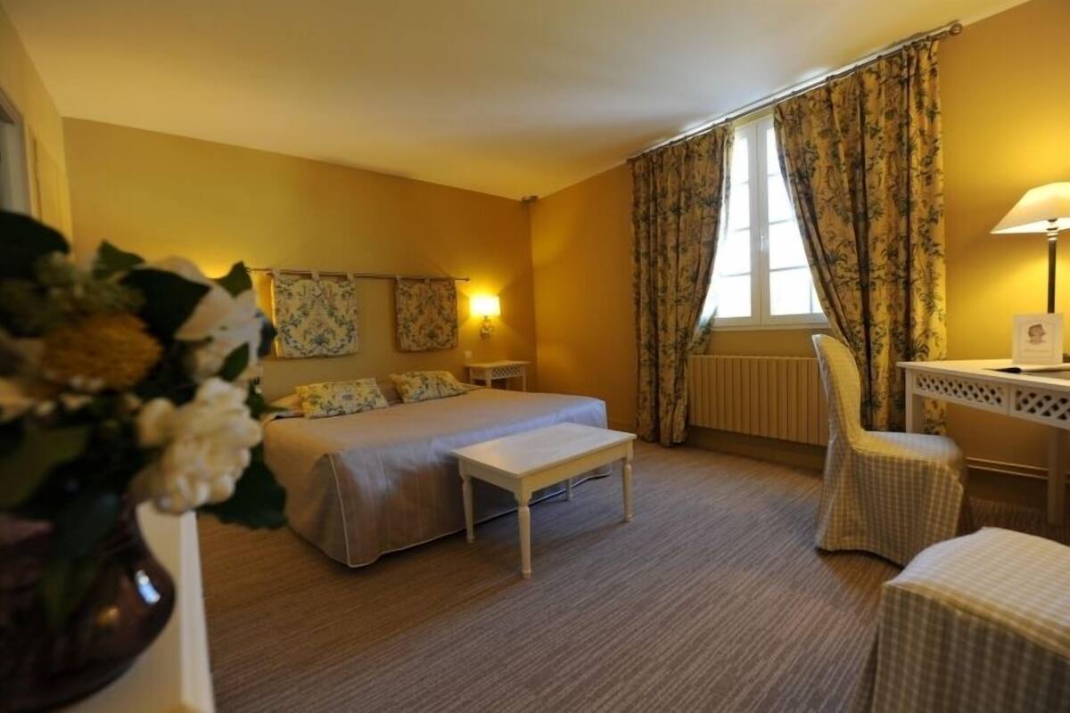 Une chambre d’hôtel avec un lit, un bureau, une chaise et une fenêtre avec des rideaux.