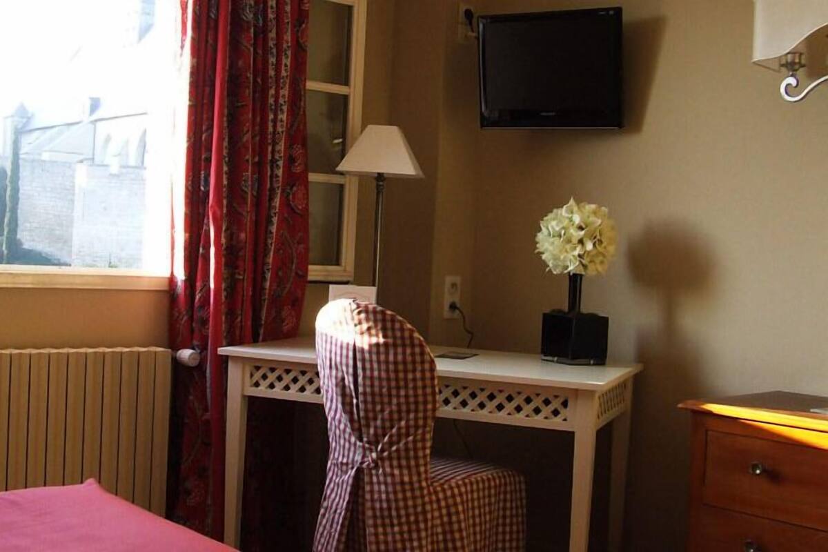 Une chambre d’hôtel comprenant un lit, un bureau avec une chaise, un téléviseur fixé au mur et une fenêtre avec des rideaux.