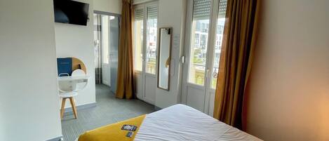 A hotel room with a bed, a desk, a television, and a window with curtains.