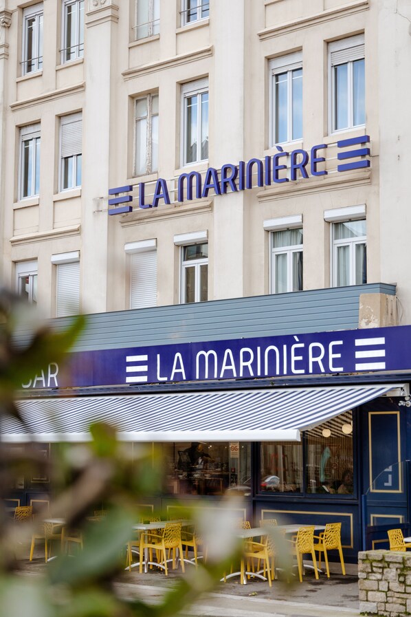 A building with a sign reading "LA MARINIERE" and outdoor seating with yellow chairs. - Cit'Hotel La Marinière (Saint-Malo)