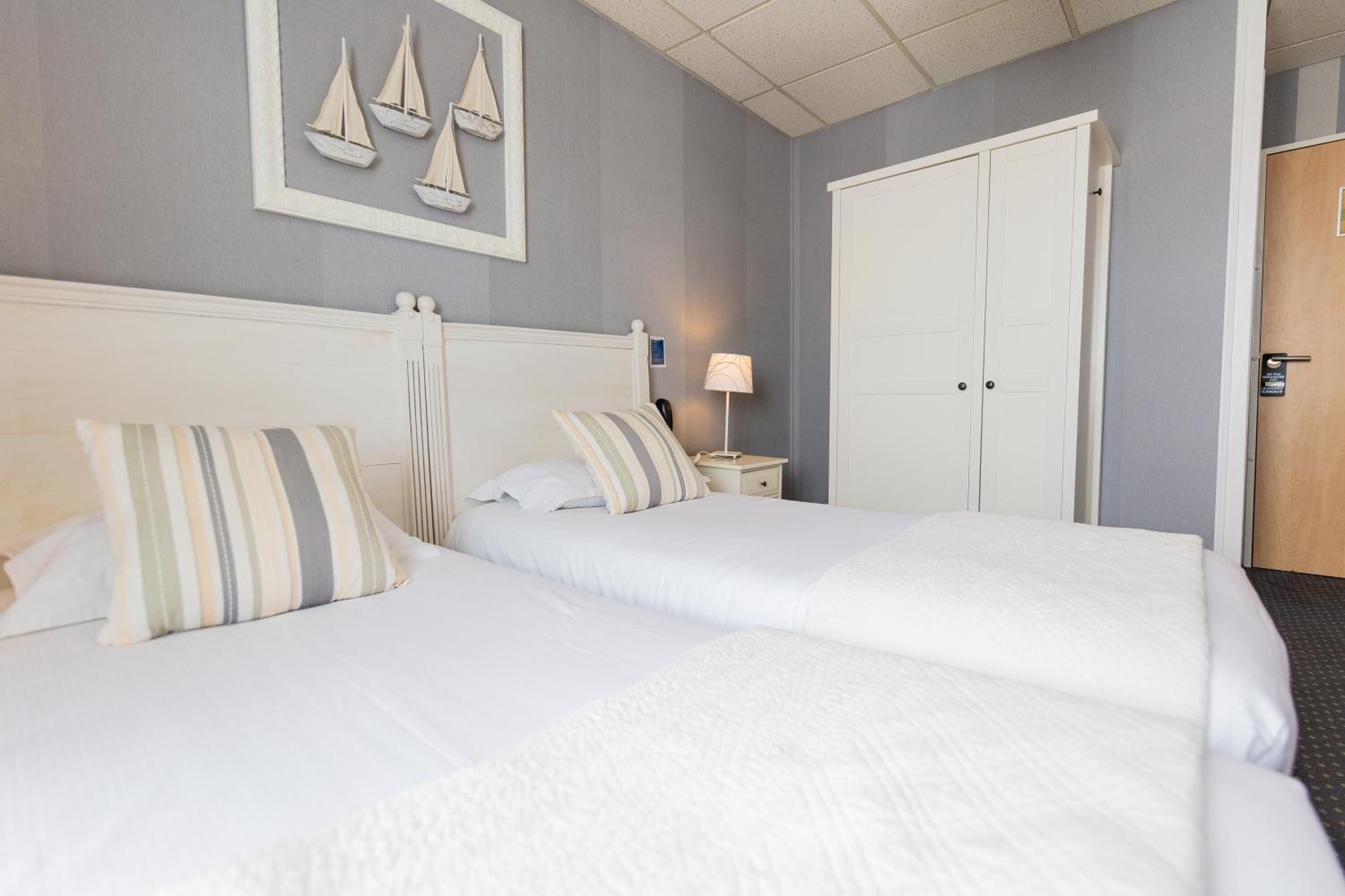 Una habitación de hotel con dos camas, una mesita de noche, una lámpara y un armario.
