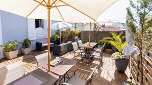 Un patio al aire libre con piso de madera, mobiliario exterior y sombrillas que dan sombra.