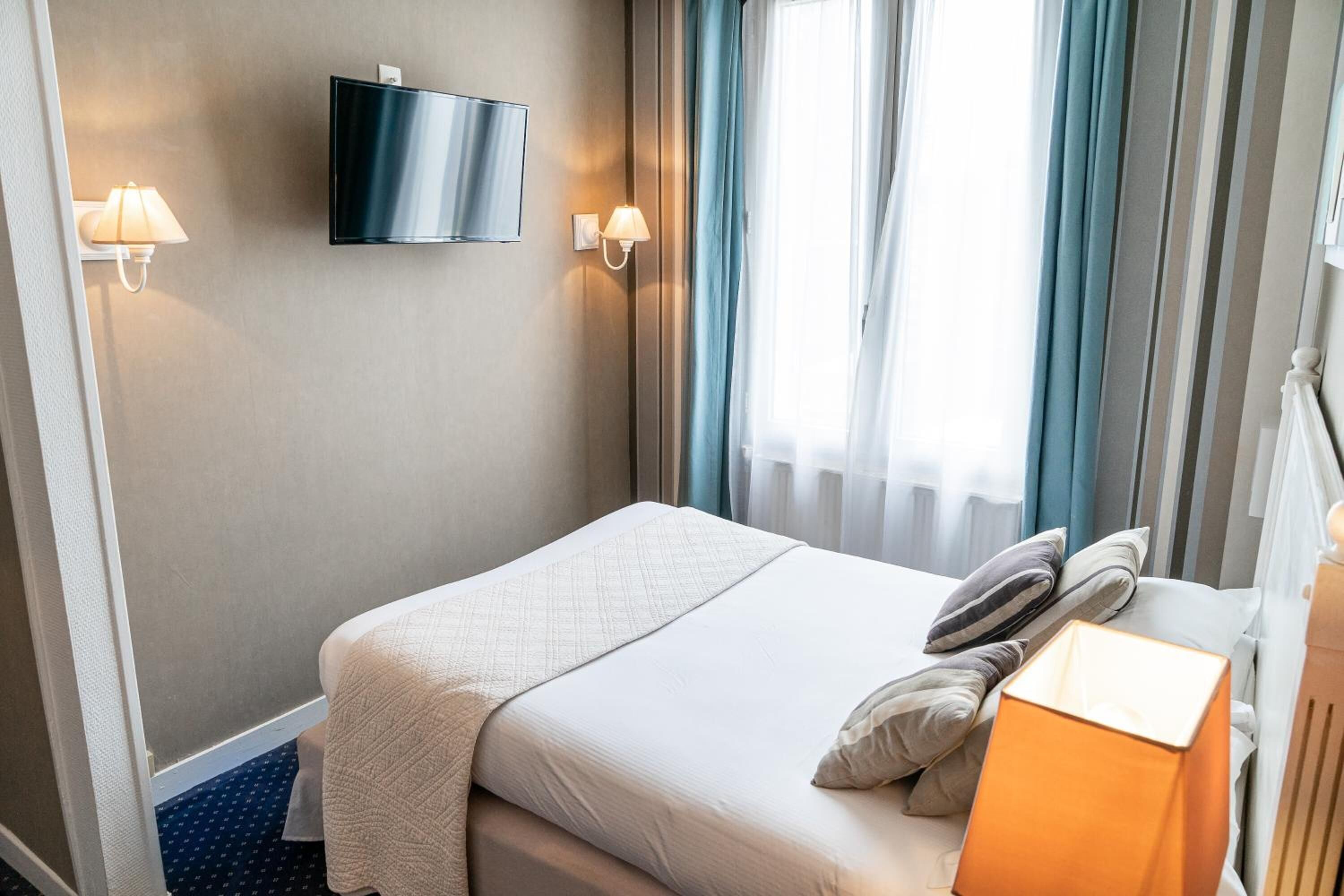 Ein Hotelzimmer mit einem Bett, einem an der Wand montierten Fernseher und zwei Wandlampen.