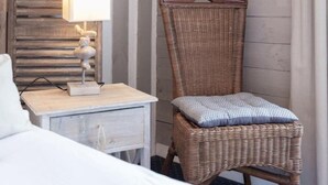 Una habitación de hotel con una cama, una mesita de noche con una lámpara, una silla de mimbre y un cuadro en la pared.
