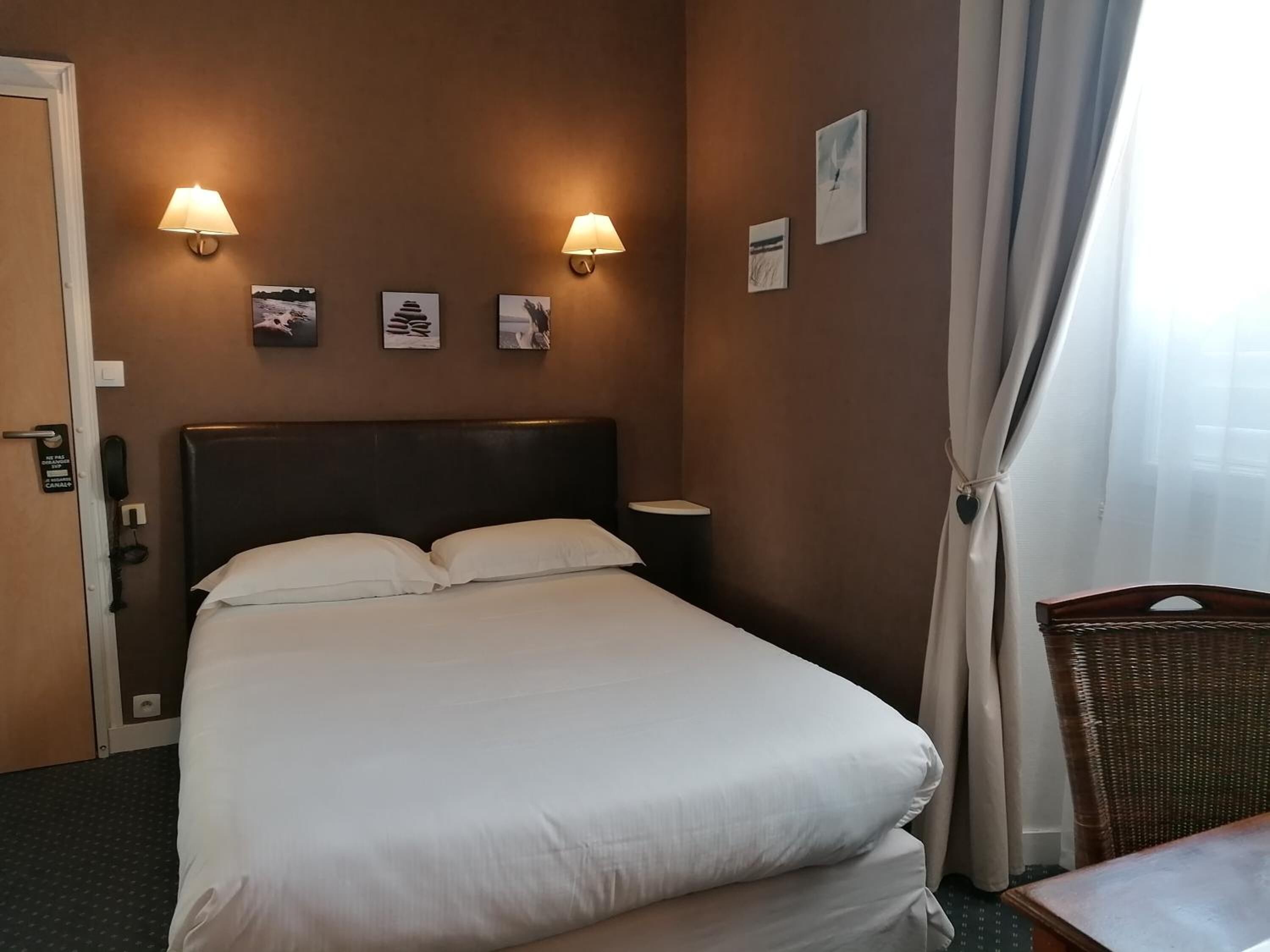 Una habitación de hotel con una cama grande, dos lámparas fijadas a la pared y una mesita pequeña.