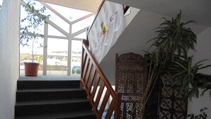 Una escalera con barandilla de madera que conduce a una plataforma. Hay una planta en maceta en la plataforma, y una pantalla decorativa de madera a la derecha.