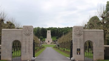 Una entrada formal con dos puertas de piedra, un camino central y un monumento al fondo.