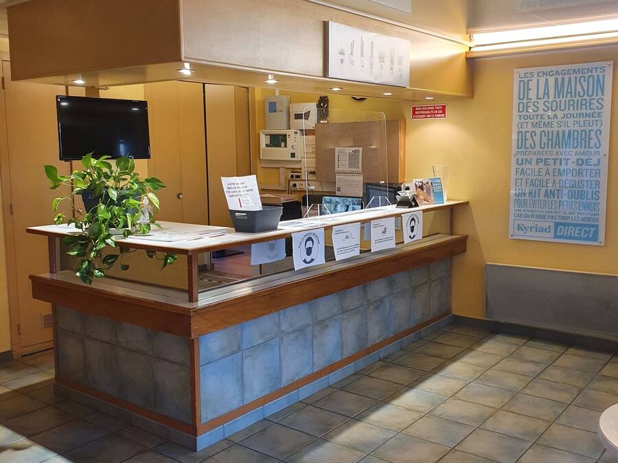 A reception desk with a potted plant, a flat-screen TV, and informational signs.