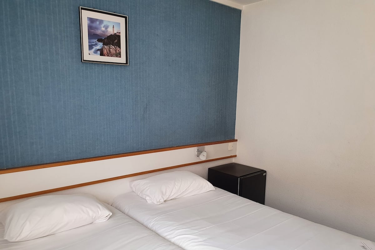 Una cama individual con ropa de cama blanca, una mesita de noche pequeña y un cuadro enmarcado en la pared.