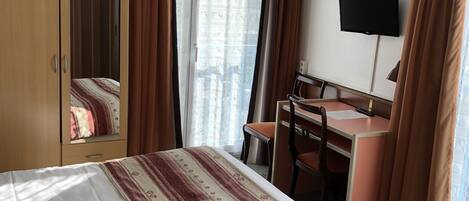 A hotel room with a bed, a desk, a chair, a TV, and a wardrobe.