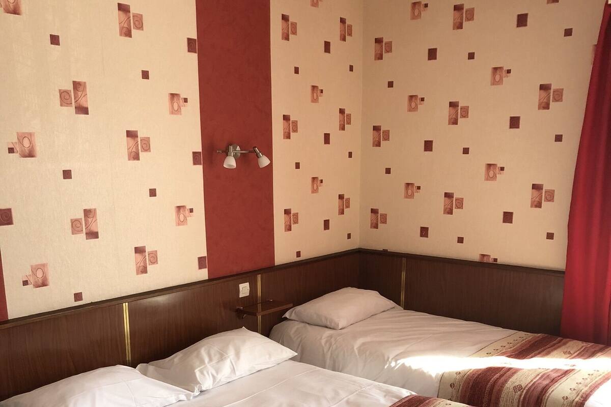 A hotel room with two beds, a wooden headboard, a red accent wall, and patterned wallpaper.