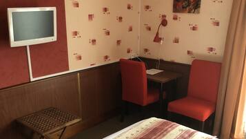 A hotel room with a bed, a desk, two chairs, a television, and a small table.
