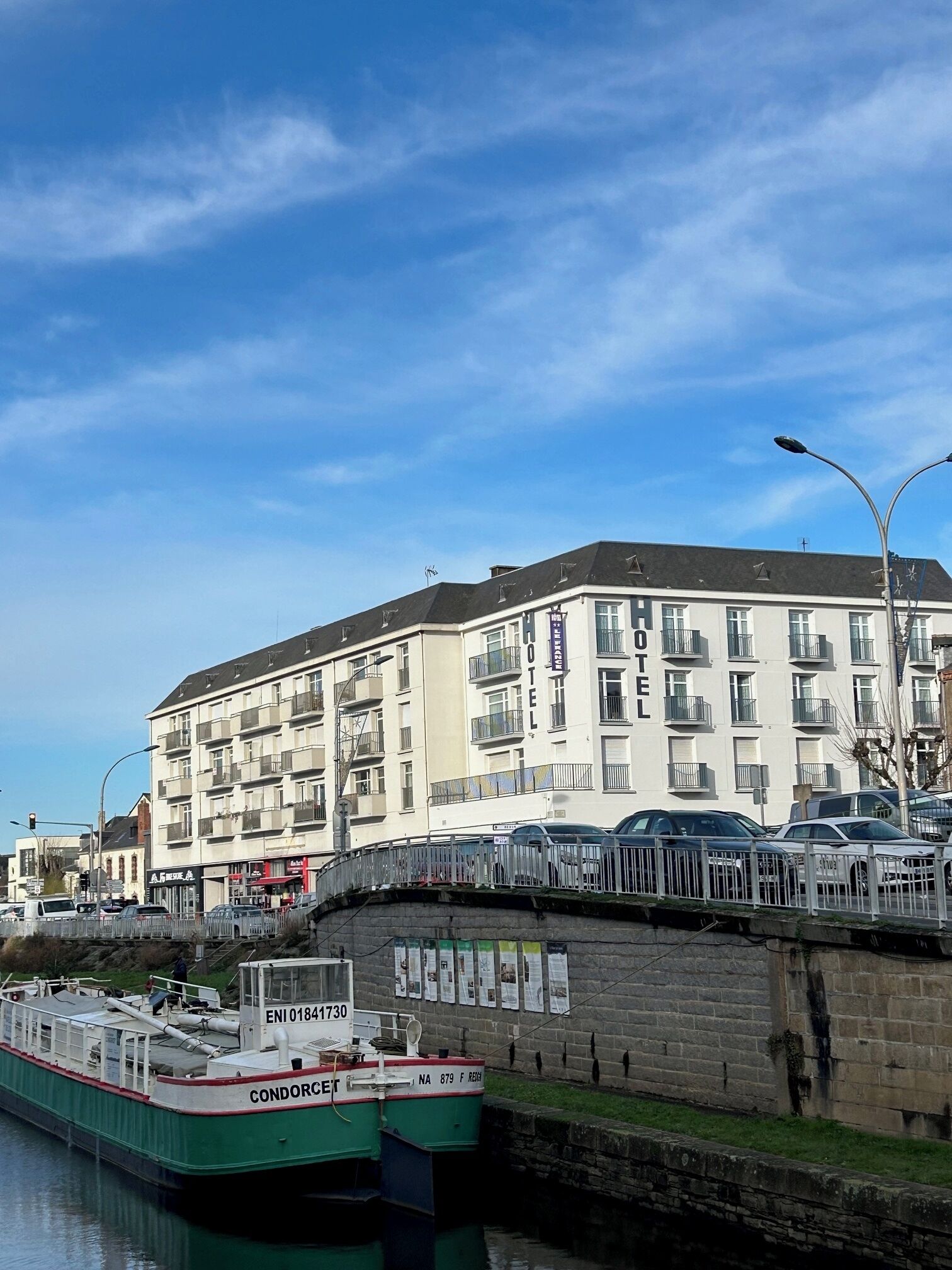 A large hotel with multiple balconies and a green boat docked nearby.