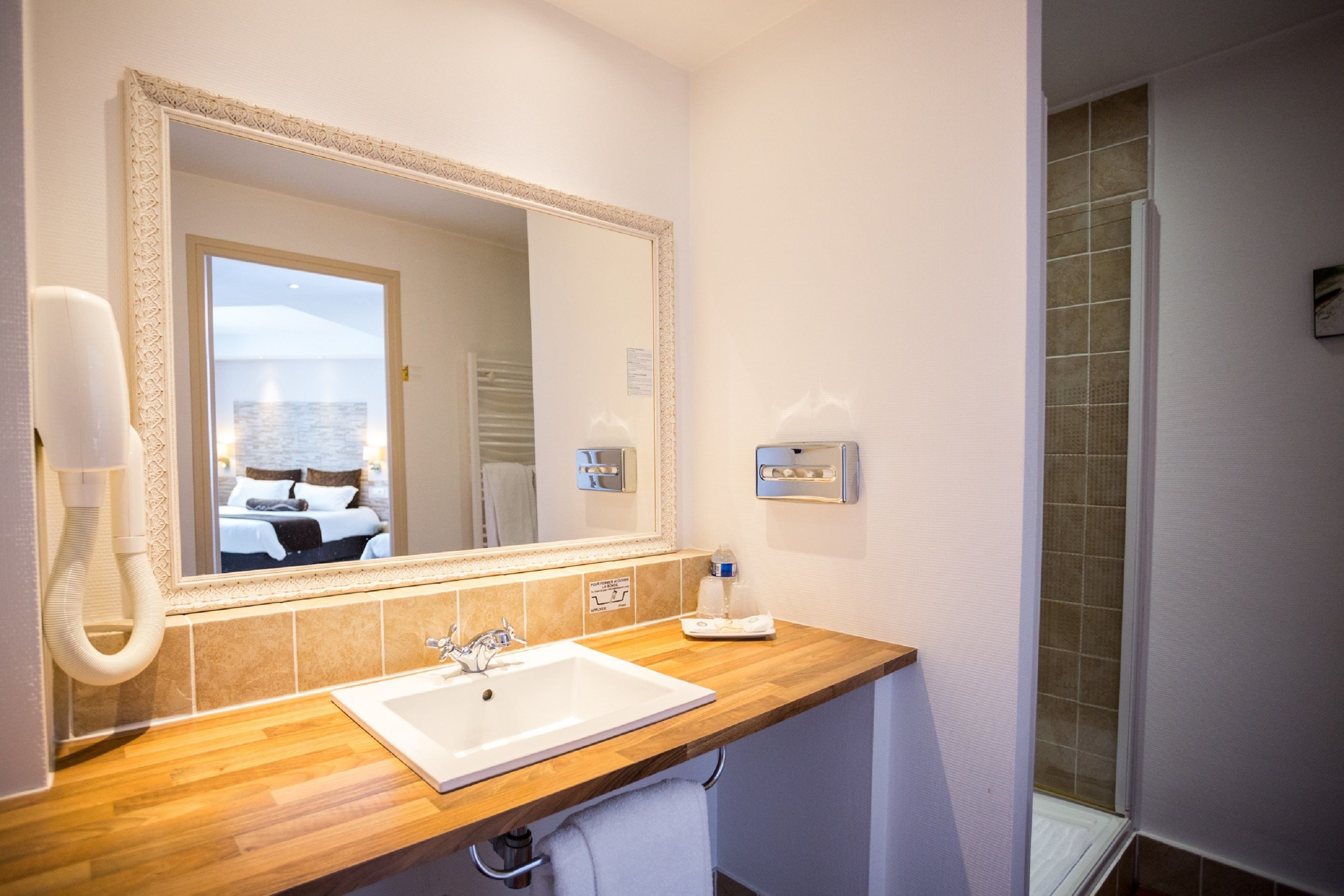 A bathroom with a wooden vanity, a large mirror, a sink, and a shower area.